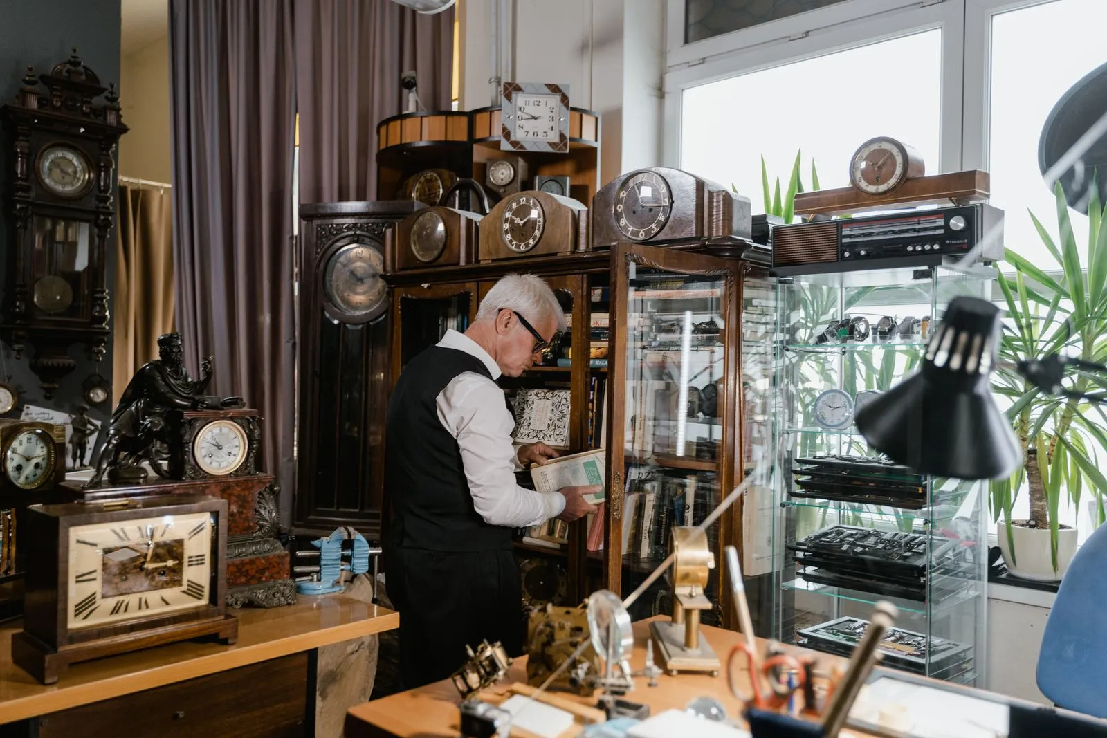 An experienced watchmaker works among antique clocks in a vintage shop setting, surrounded by classic timepieces.